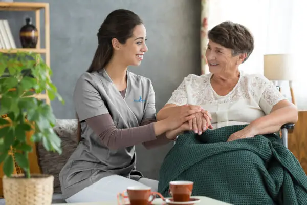 Carer kneeling beside an elderly patient. Patient is sitting on a wheelchair.