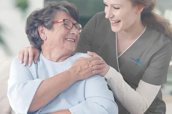 Carer placing her hands on an elderly patient's shoulder. Eldery patient is sitting on a wheelchair.