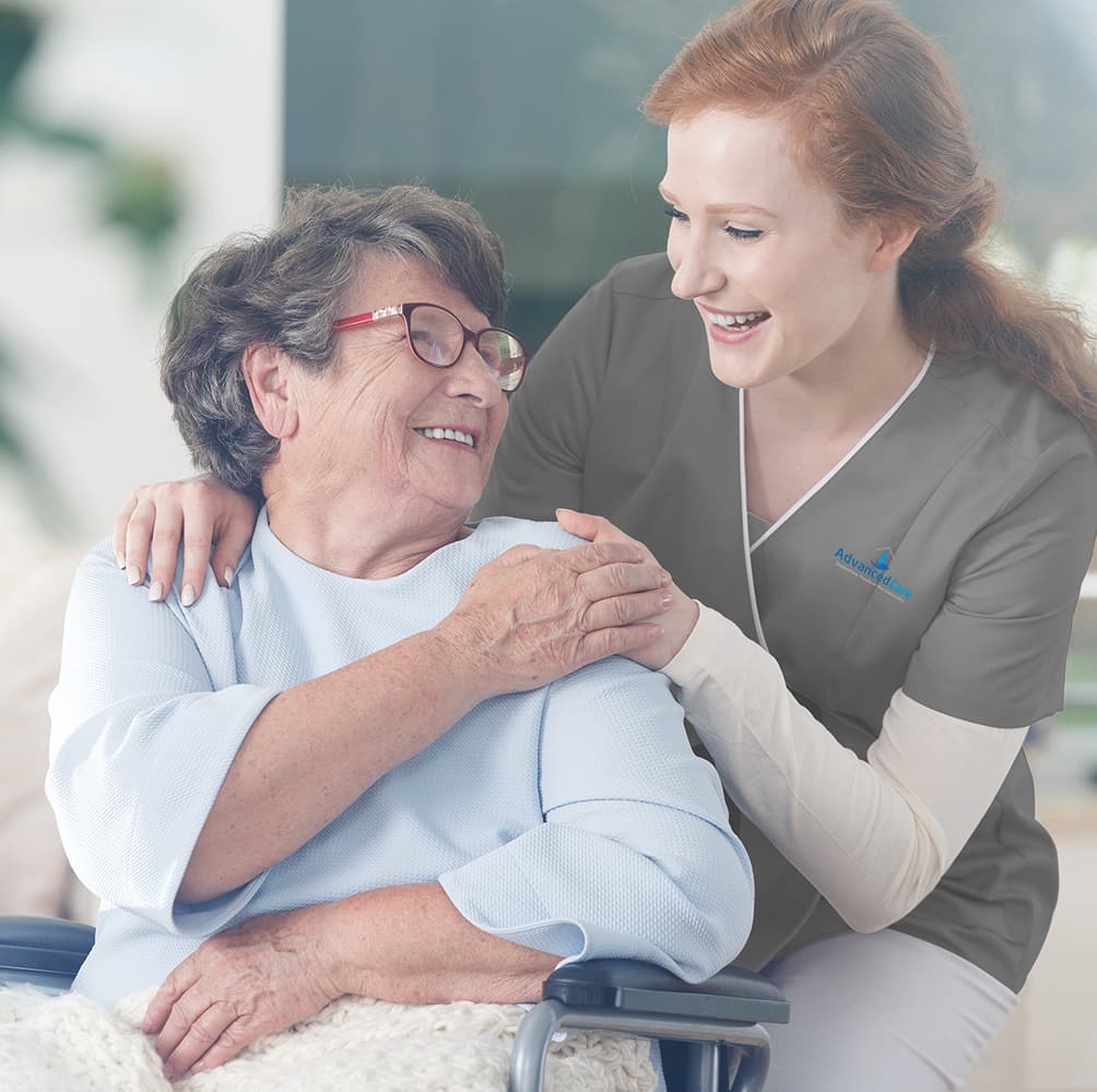A home care worker kneeling beside an elderly patient. Patient is sitting on a wheelchair.